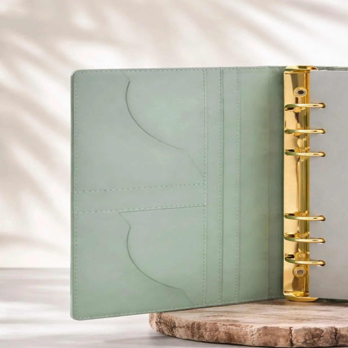 Notizbuch Binder im A5-Format mit salbeigrünem Einband aus glattem Material, dezenter Naht und goldener Ringmechanik.