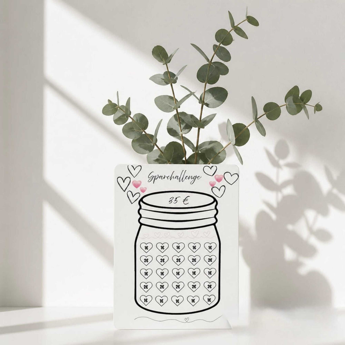 Sparglas Challenge 35€ als weißer Sparplan-Ausdruck aus mattem Papier mit schwarzer Glaszeichnung und rosa Herzen.