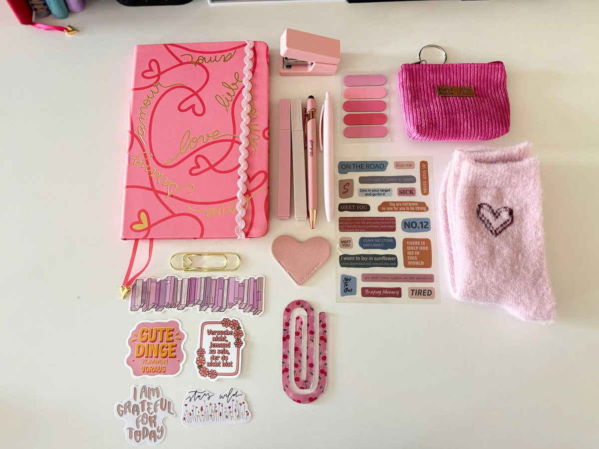 Notizbuch A5 in kräftigem Rosa mit goldenen Schriftzügen und Wellenrand, ergänzt durch Stifte, Sticker und Accessoires